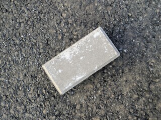 Close-up of a single weathered brick placed on asphalt background