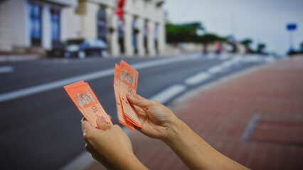 Hands holding malaysian ringgits outdoors on a city street reflecting financial transactions and...