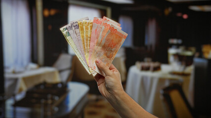 Hand holding philippine pesos inside a stylish restaurant showcasing financial readiness and...
