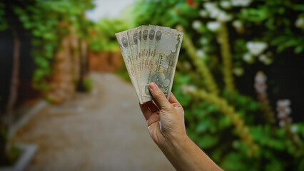 Man holds uae dirham banknotes outdoors in a lush park setting, symbolizing financial prosperity...