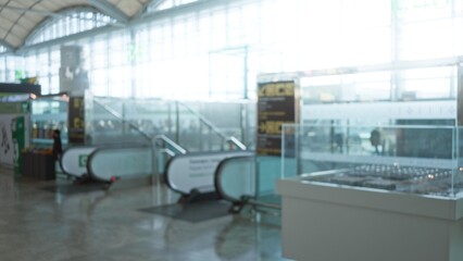 Naklejka premium Bokeh airport terminal showing blurred interiors with people and escalator in the background under bright light in a busy international travel hub.