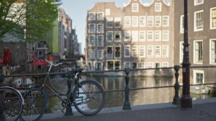 Blurred bicycle and canal in amsterdam with historic buildings softly focused in the background under a sunny sky.