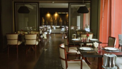 Elegant restaurant with blurred dining area featuring defocused tables and ambient lighting, creating a warm, inviting atmosphere for patrons seeking a sophisticated dining experience.