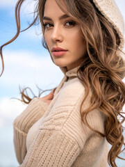 A woman in a beige hoodie, exuding warmth and style, with a gentle smile on her face. Walking on the beach on a windy cool summer day. 