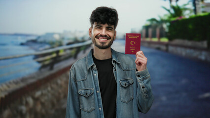 Young man holding turkish passport on seaside promenade with ocean view and outdoor setting,...