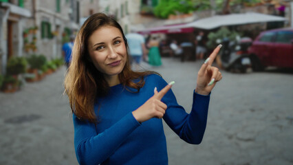 Woman smiling in blue sweater pointing on a bustling city street with blurred background, capturing...