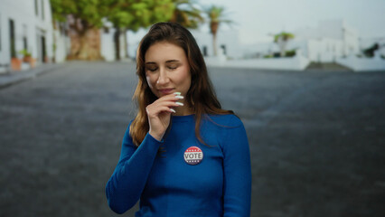 Woman wearing vote badge smiles confidently on a city street, representing civic engagement in the...