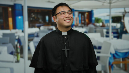 Smiling priest standing in an outdoor restaurant with blurred background of tables and people...