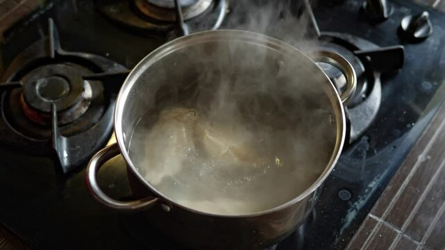 A close-up shot captures the domestic and active mood as a hand stirs dumplings or pierogi in a pot of boiling water on a gas stove, with steam rising, showcasing home cooking