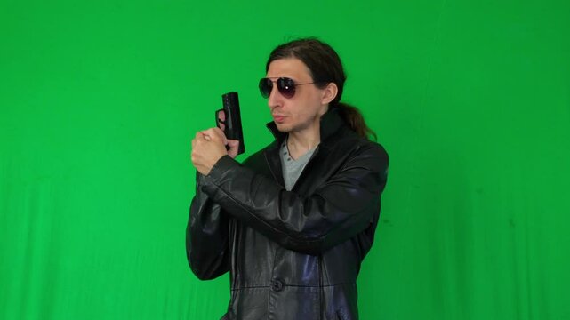 A mid-shot captures a serious and action-oriented mood as a man in a leather jacket and sunglasses holds a handgun, ready for action, against a green screen, perfect for diverse themes