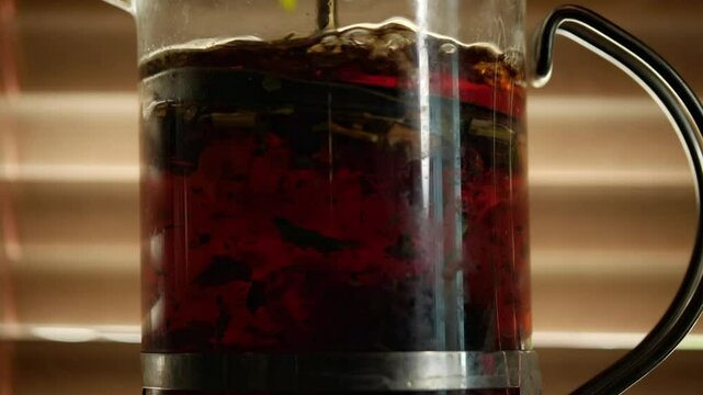 A macro shot captures the rich, vibrant mood of red tea with visible loose leaves swirling as it brews in a French press, showcasing its beautiful color and texture against a softly lit background