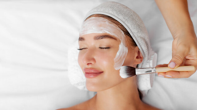 Perfect touch of brush. Beautiful lady with soothing pampering cosmetic facial mask for fresh clear skin lying in beauty parlor, panorama, free space, top view