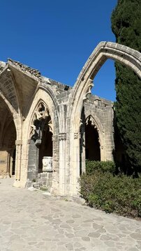 Stone Gothic arches from the historic Bellapais Abbey, surrounded by tall cypress trees and medieval architecture under a clear sky in Cyprus. High quality 4k footage