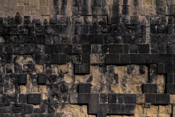 Close-up of dark textured stone wall with black rectangular blocks. Ideal for architectural presentations, construction brochures, or design mockups needing rugged texture.