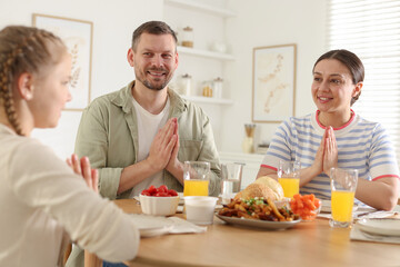 Family praying together before dinner at table indoors