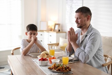Father and son praying before dinner at table indoors