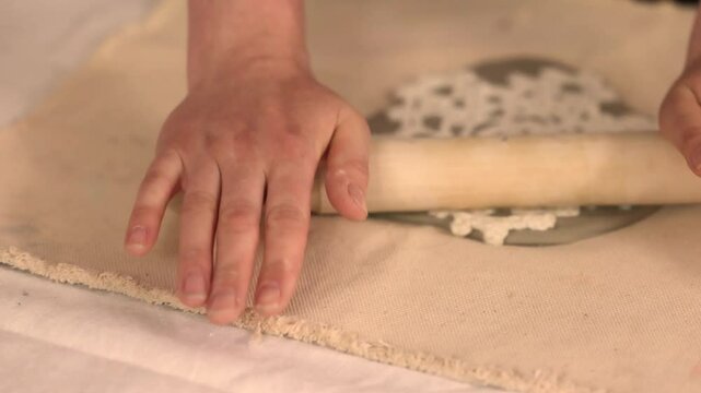 Handcrafting ceramic Christmas decorations in a pottery studio. Using fabric snowflake stencil and rolling pin to imprint festive patterns on clay. Creative and cozy holiday preparation.