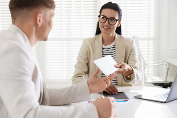 Money bonus. Employee receiving envelope from boss in office