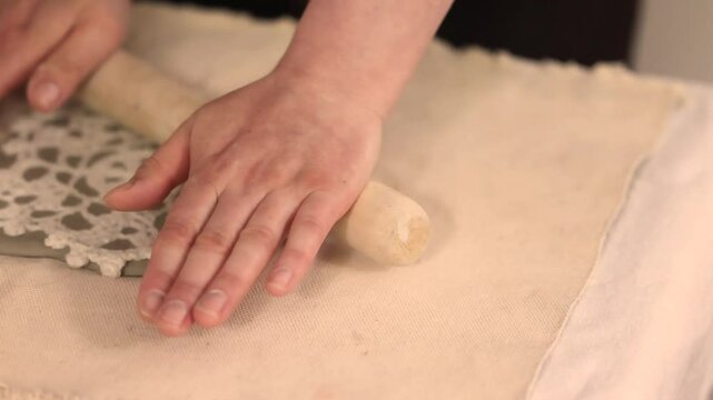 Handcrafting ceramic Christmas decorations in a pottery studio. Using fabric snowflake stencil and rolling pin to imprint festive patterns on clay. Creative and cozy holiday preparation.