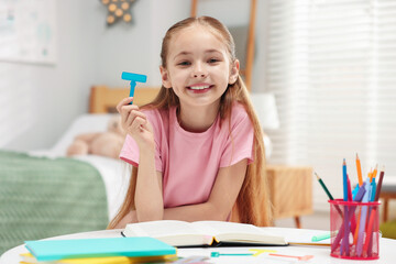 Dyslexia. Little girl holding letter T at table indoors