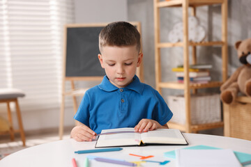 Dyslexia. Little boy reading book at table indoors