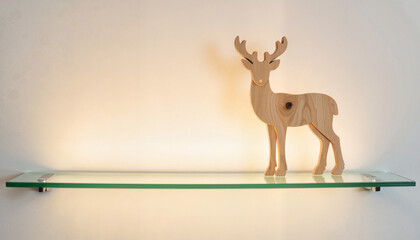 Fototapeta premium Wooden deer figurine displayed on a glass shelf against a wall 
