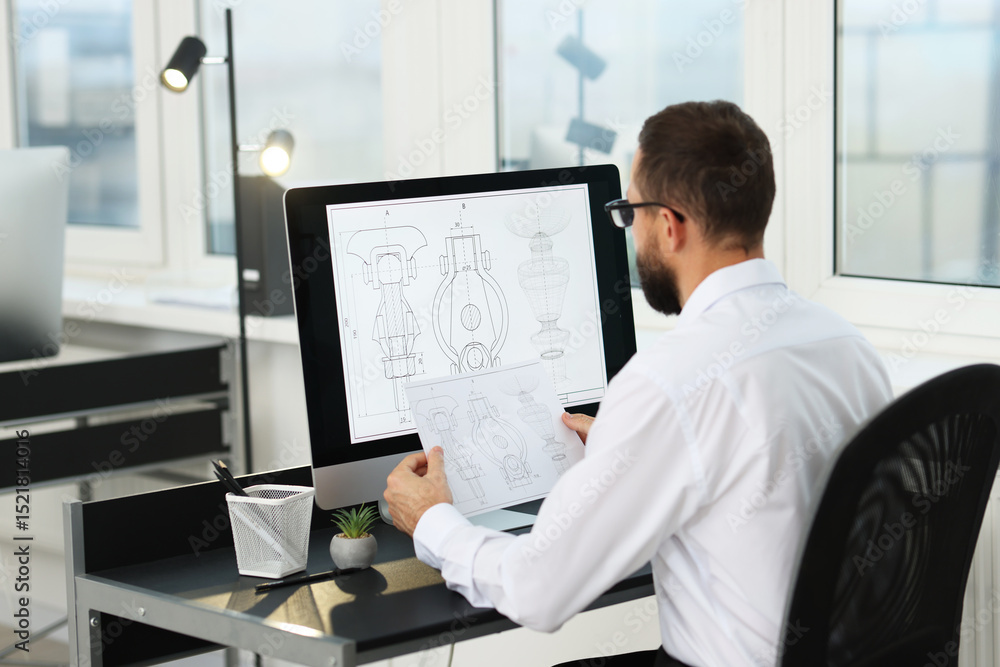 Poster technician making digital engineering drawing on computer at desk in office, back view