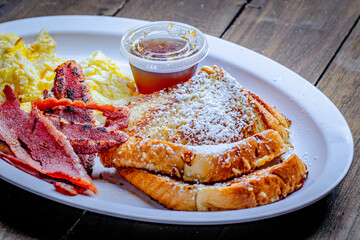 pancakes with egg and bacon breakfast served with a side of syrup.