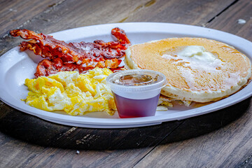 egg and bacon with pancake breakfast served sweet syrup in a white plate.