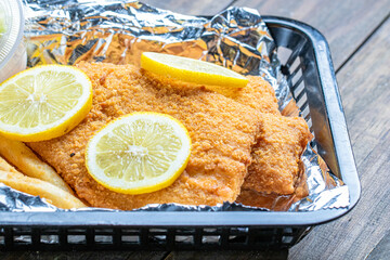 Tasty fried fish fillet in a serving box with slices of lemon on the top for decoration.