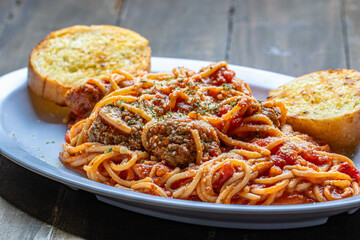 Tasty pasta with meatball and tomato sauce with slices of garlic toasts served in a white plate.