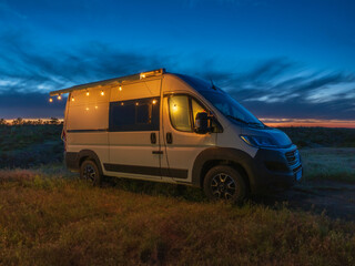 view to white camper van with night lights in twilight night sky with copy space
