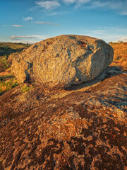 portrait view to alone granite boulder in sunset light under blue sky