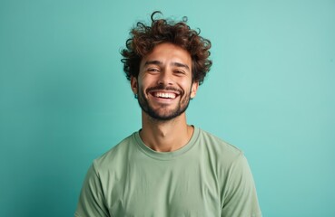 Obraz premium Cheerful young man portrait against turquoise background. Happy caucasian male face with white teeth smile, with curly hair. Casual look. Smiling person expresses positive emotions. Success concept.