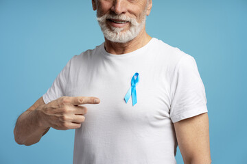 Senior man pointing at blue ribbon supporting prostate cancer awareness
