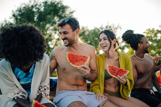 Happy friends enjoying watermelon by the poolside on summer vacation - Powered by Adobe
