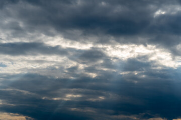 Dark clouds fill the sky with patches of light as the sun sets, creating a dramatic atmosphere. The scene captures a moment of transition before nightfall