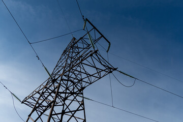 A power transmission tower stands tall against a clear blue sky, with overhead power lines extending in multiple directions on a sunny day