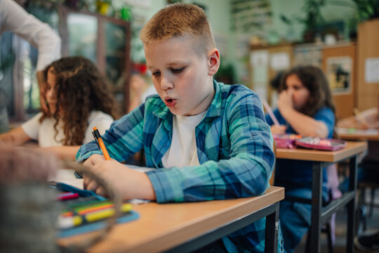 Elementary school student writing during class at school desk