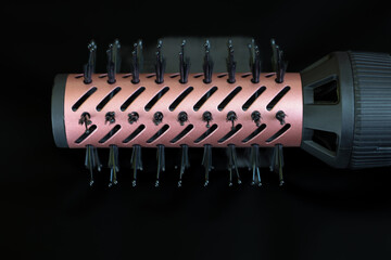 Macro shot of a cylindrical hair styling attachment with a metallic surface and black bristles. The...