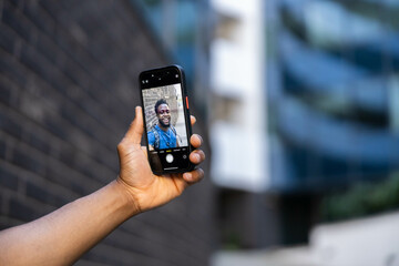A close-up view of a man capturing his smiling selfie, showcasing connection through technology and personal expression. Selective focus on phone screen