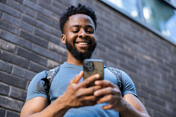 A young man happily interacting with his smartphone, showcasing joy and engagement in an urban setting with a brick wall backdrop.