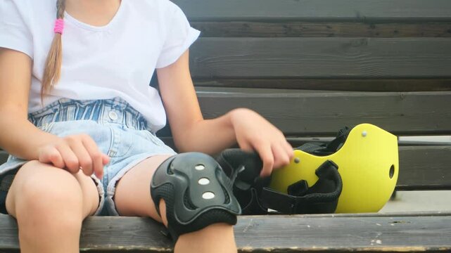 Young skater girl putting on protective shin guards and knee pads for skating. child rollerblader preparing for a ride in skatepark in summer