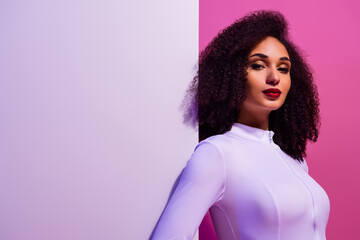 Confident young woman posing against vibrant pink and purple backdrop, exuding elegance and charm in a trendy outfit