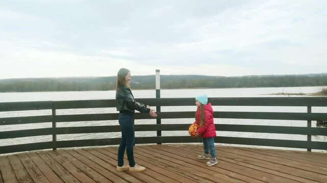 Mother and daughter at the pier near the water having fun. Mom with little girl playing a ball