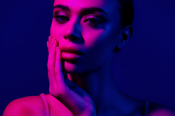 Portrait of a young woman in moody ultraviolet pink and blue light evoking an artistic and...