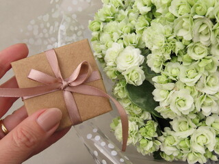 Woman hand holding a gift box with pink bow over a white calandiva arrangement. Gift and flowers.