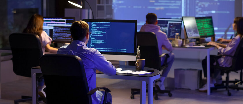 Team of programmers working in office at night, back view