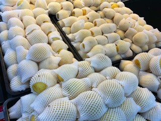 A close-up of neatly arranged yellow pears wrapped in white foam netting, ready for sale at a market or grocery store.
