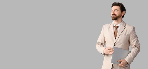 Handsome businessman in stylish beige suit  holding laptop on grey background with space for text